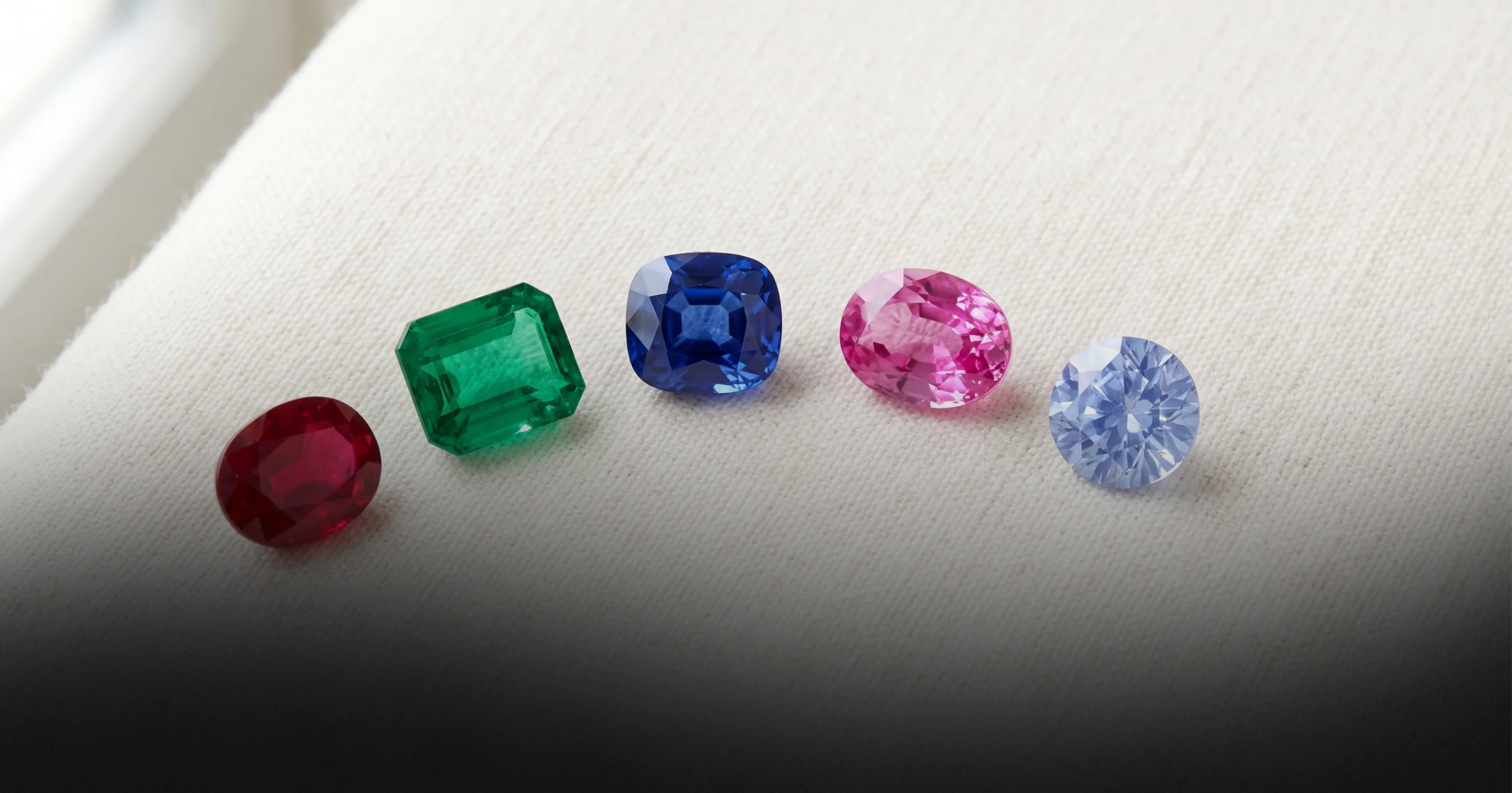Five loose stones of different colours arranged in a row — ruby, emerald, sapphire, pink sapphire and diamond — illustrating choice by colour.