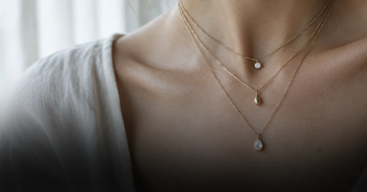 Close-up of a woman's neck wearing three layered gold necklaces of different lengths, each with a small pendant.